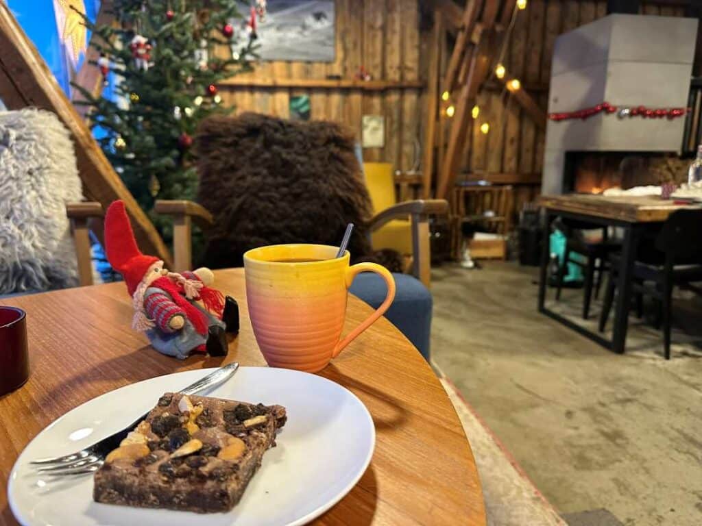 A cafe table with sweet pastry and coffee, Christmas decorations, wooden details, and a fireplace in the background