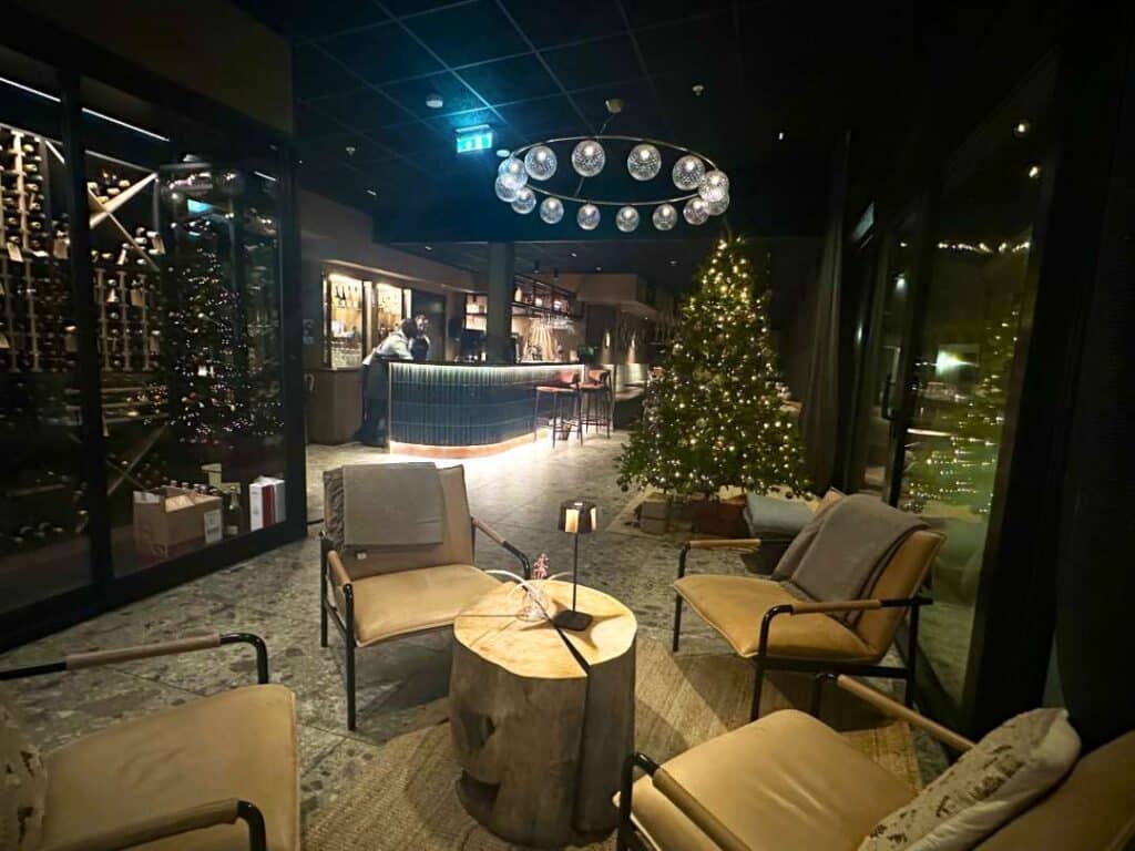 Cozy foyer with warm lighting, a seating area, glittering christmas tree, and a bar at the end of the room at night