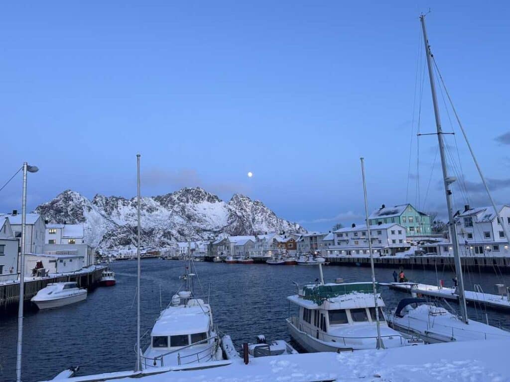 A snow covered harbor in the Arctic blue light with white wooden houses around fishing boats in dock in the winter in Lofoten Norway
