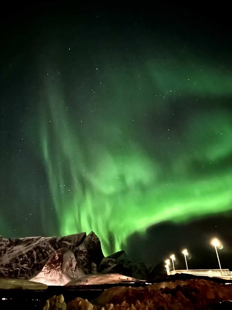 Spectacular green northern lights in a spectacular pattern across the sky over majestic snow covered mountains in Lofoten Norway, by one of the many bridges connecting the islands in Lofoten, you can even see the stars through the green vail of light in the sky. 