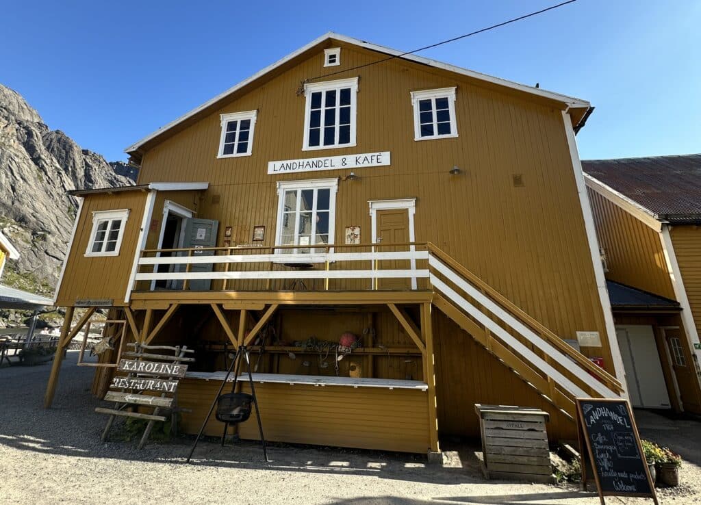 An old yellow wooden traditional house with white window sills, that under a blue summer sky, home to a charming traditional old fashioned shop and cafe in Nusfjord, Lofoten, Norway