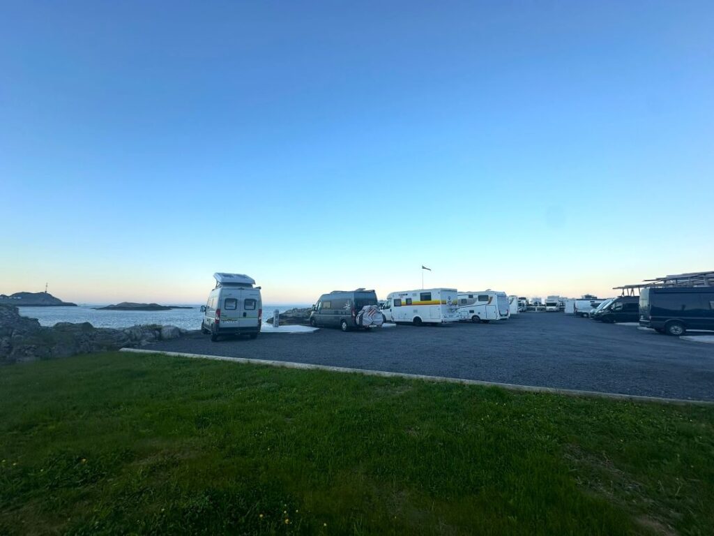 A camper van parking space next to the West Fjord in Lofoten Norway, where you pay to park next to the sea, under the clear blue midnight sun night sky with infinite ocean views