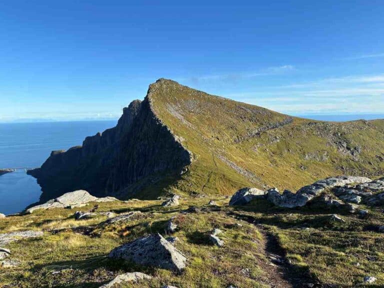 Path to a mountain ridge over the vast blue ocean under clear blue sky on a sunny September day in Lofoten Norway