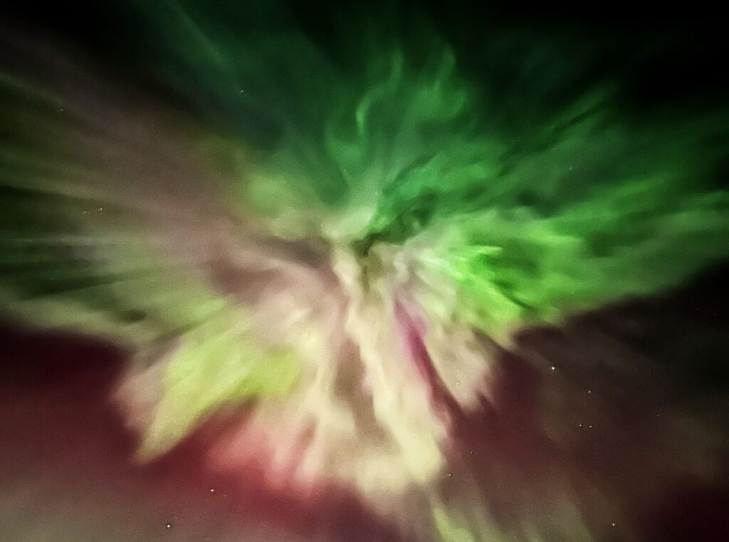 An explotion of colors in green white, yellow, pink and purple, northern lights dancing in a star pattern across the night sky