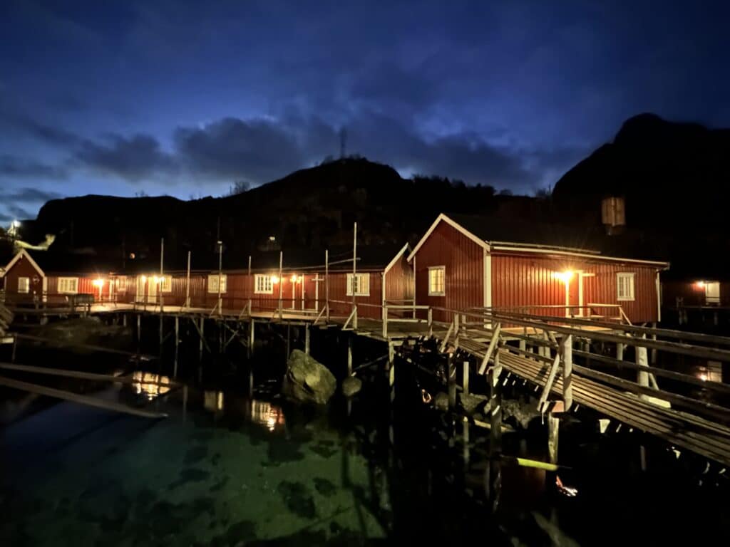 Red fishermans cabins at night in Lofoten, the sea blank and transparent under the wooden cabins, and the darkening sky still has a blue tone behind dark mountains