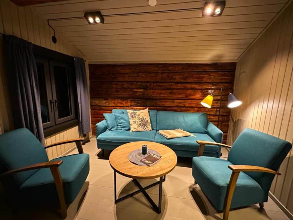 Blue sofa and charis in a warmly lit cabin at night with the old wooden wall from 100 years old wooden fishermans cabin at Svinøya rorbuer in Svolvær Norway.