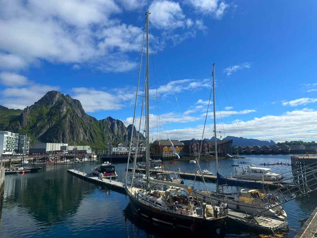 Sail boat by the dock on a bland sea with a backdrop of majestic mountains under a blue summer sky in Svolvær Lofoten Norway.
