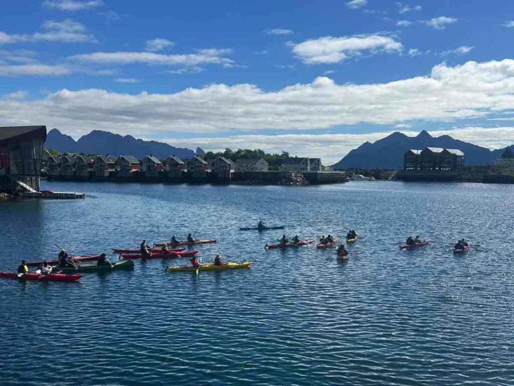 A group of kayakers ready to go from the Svolvær harbor in Lofoten, surrounded by old fishermans cabins under a blue summer sky